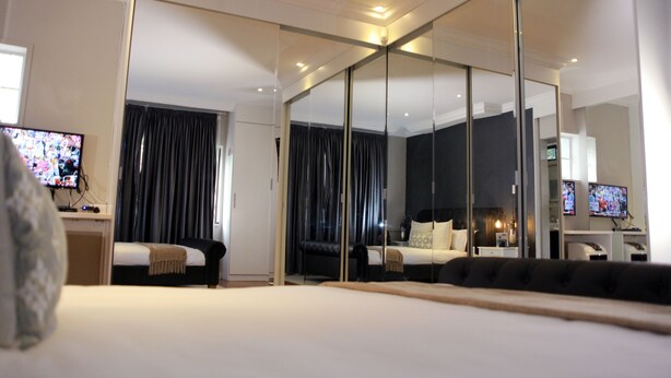 Une chambre d’hôtel moderne dotée d’un grand lit, d’un bureau avec une télévision, d’un coin salon avec un canapé et d’un grand miroir.
