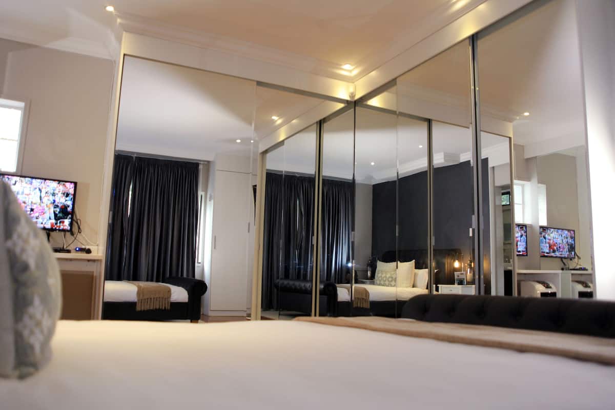 Ein modernes Hotelzimmer mit einem großen Bett, einem Schreibtisch mit Fernseher, einer Sitzecke mit Sofa und einem großen Spiegel.