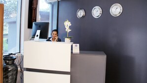 Un comptoir d’accueil avec un ordinateur, un vase de fleurs et trois horloges au mur.