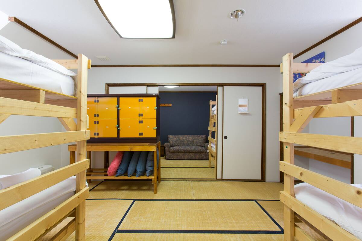 A dormitory room with bunk beds, a wardrobe, and a futon bed.