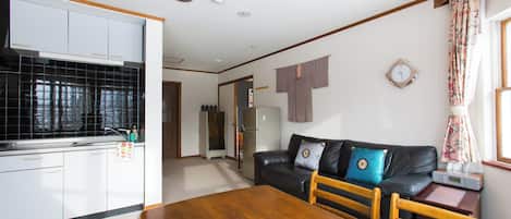 Una cocina con armarios blancos, una mesa de comedor con sillas, un sofá de cuero negro con cojines y un reloj en la pared.