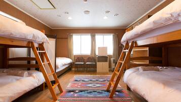 A dormitory room with bunk beds, a desk, chairs, and a patterned rug.