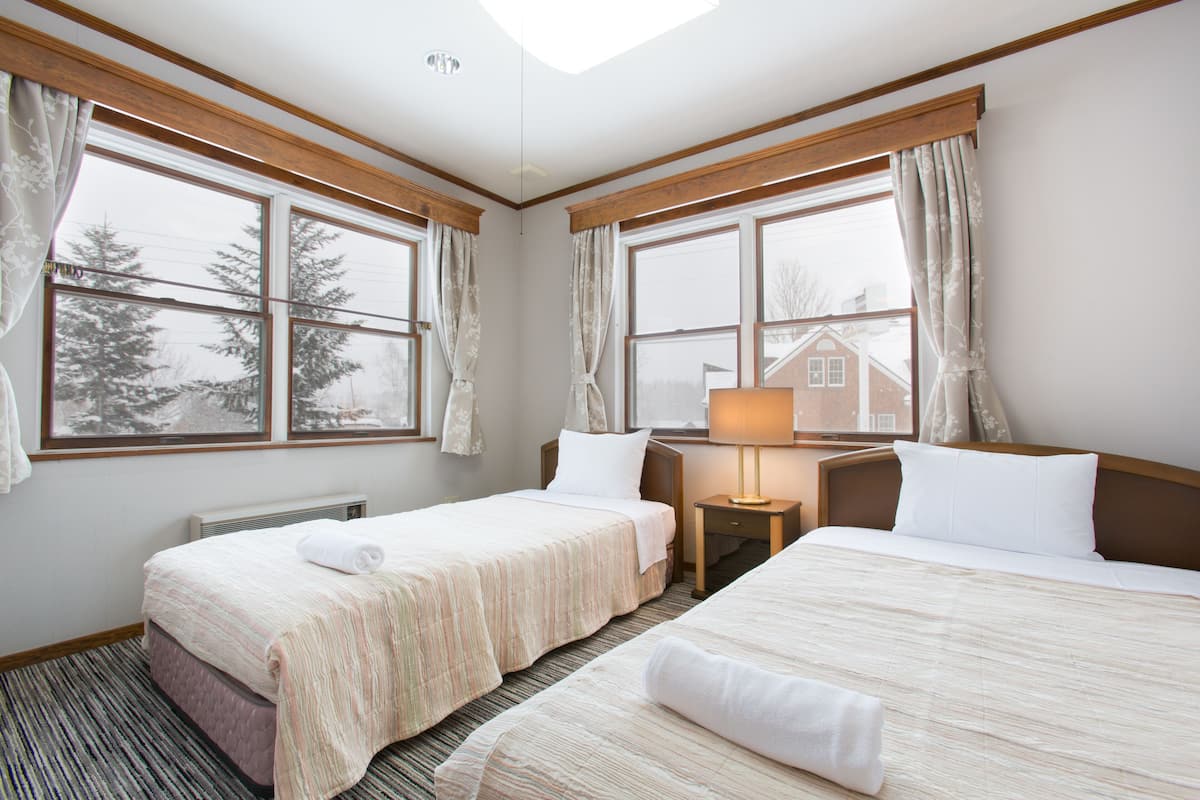 A hotel room with two beds, a window with curtains, a lamp, and a radiator.