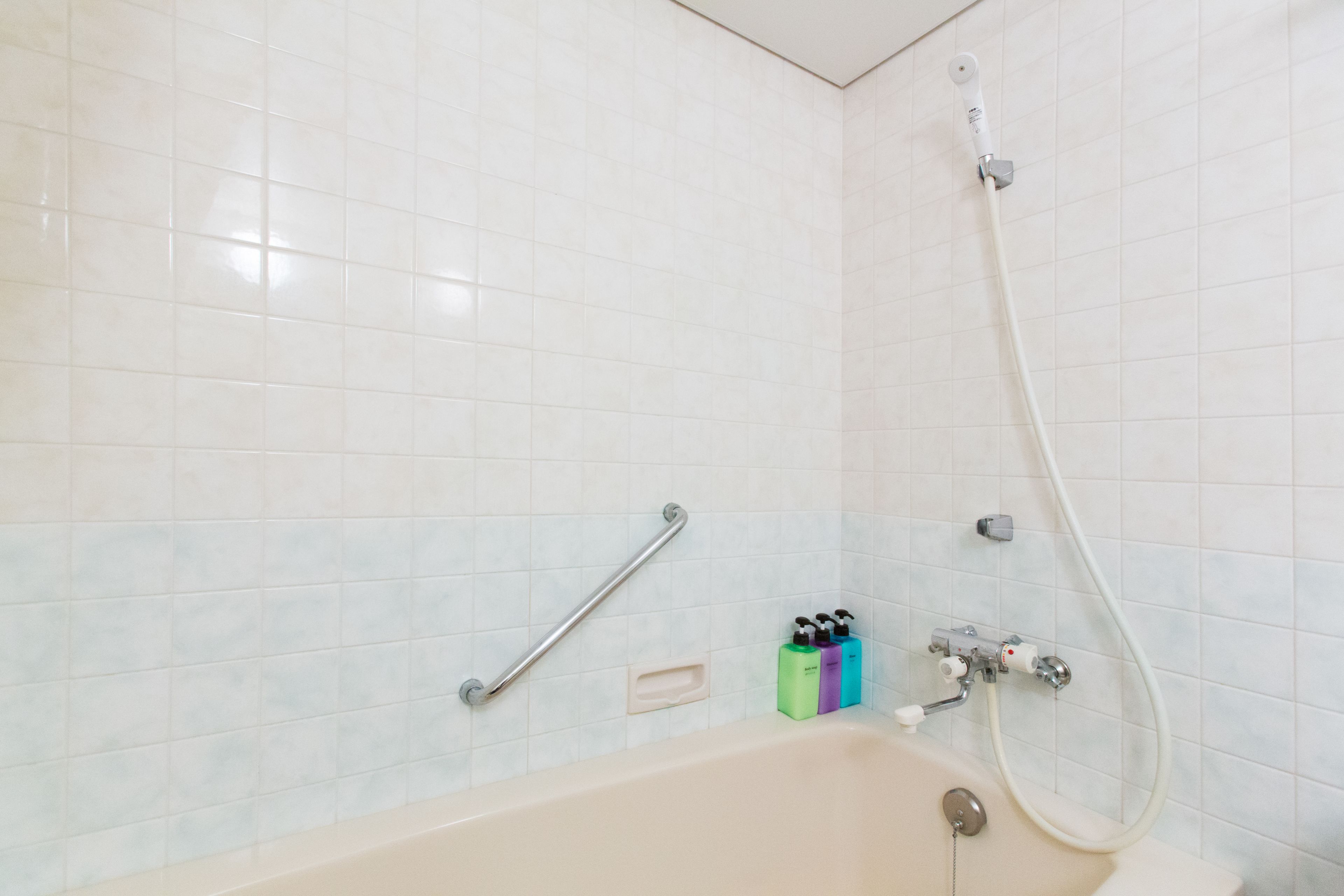 A bathroom with a bathtub, a shower, and a handrail.