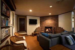 A living room with a brick fireplace, a television mounted on the wall, and a sofa with cushions. - Ramat Niseko  (Kutchan)