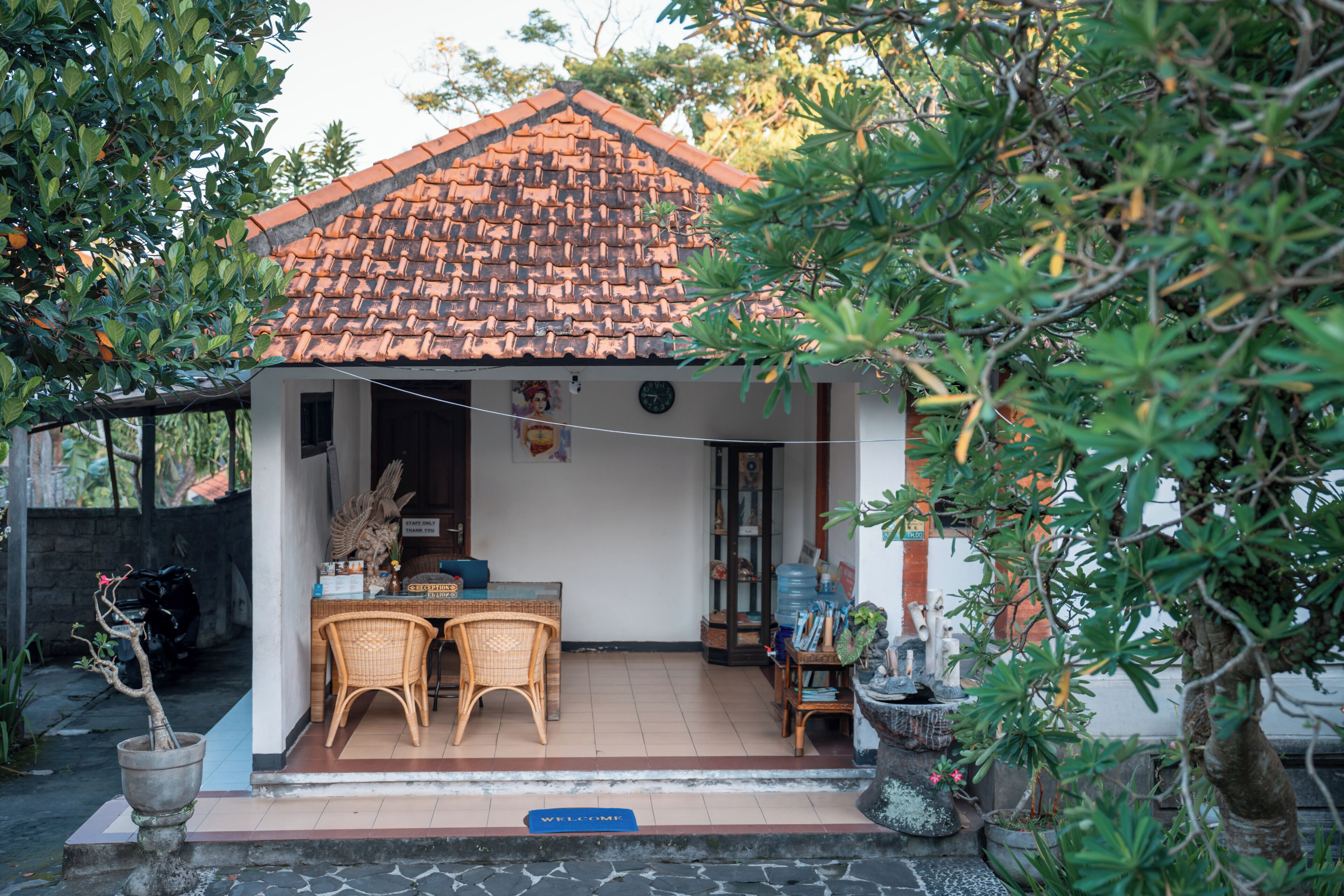 Een huis met pannendak, deurmat, een eethoek met stoelen en een bloempot.