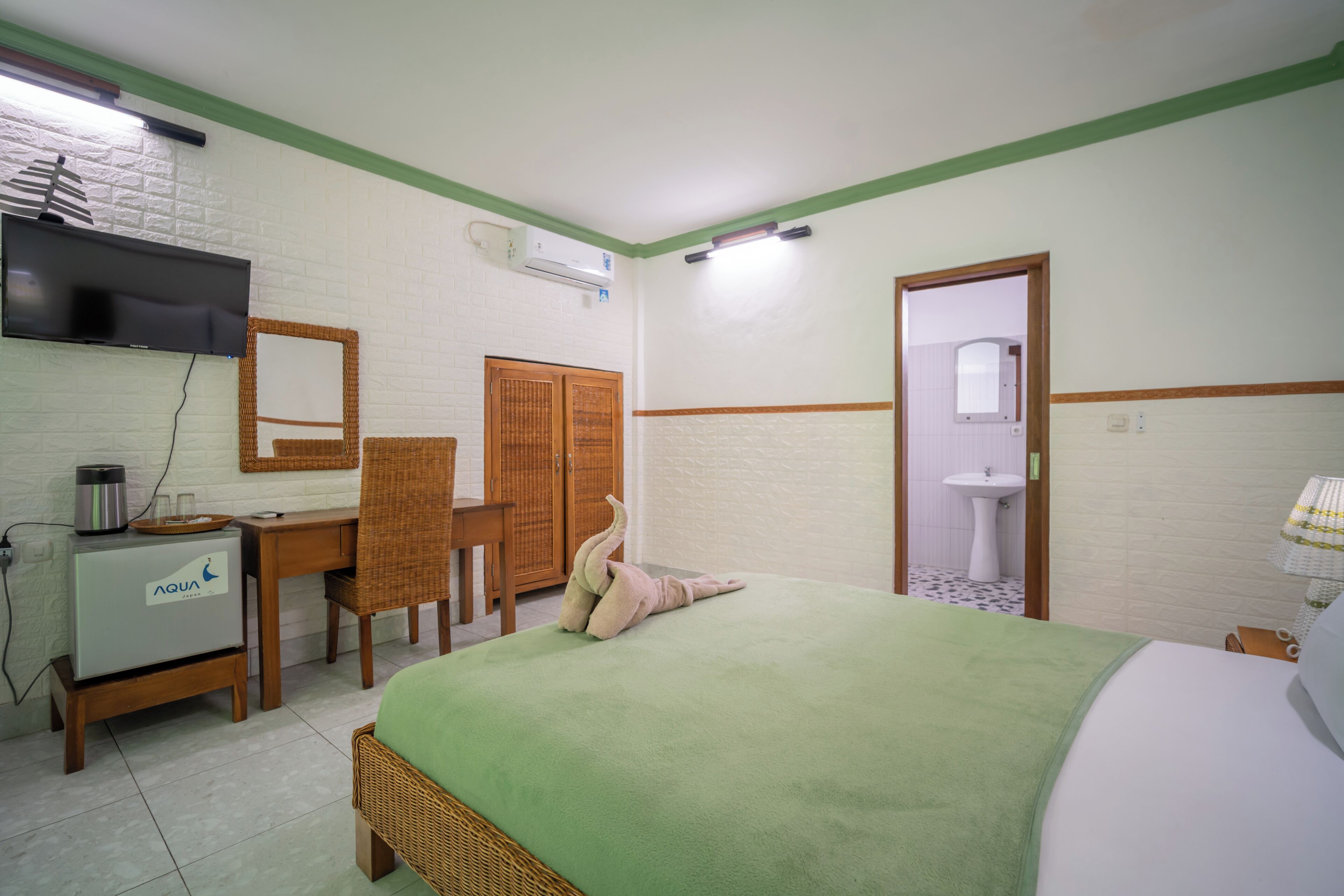 A hotel room with a bed, a desk with a computer, a television, a wardrobe, and a bathroom.