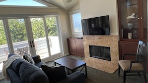 A spacious living room with a fireplace, a flat-screen TV mounted above it, a comfortable sofa, and a dining table. - Perfect Laguna Beach Vacation-ocean views/beach across street/town 1 block (Laguna Beach)