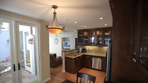 A modern kitchen with wooden cabinets, a stainless steel dishwasher, and a dining area with a table and chairs. - Perfect Laguna Beach Vacation-ocean views/beach across street/town 1 block (Laguna Beach)