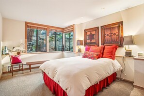 Relax in a spacious bedroom with a large bed, wooden chair, and picture frames, offering a view of the outdoors.