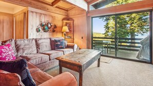 Ein gemütliches Zimmer mit Holzvertäfelung, einer Ledersofa, einem Holztisch und Blick auf eine Terrasse mit Gartenmöbeln.