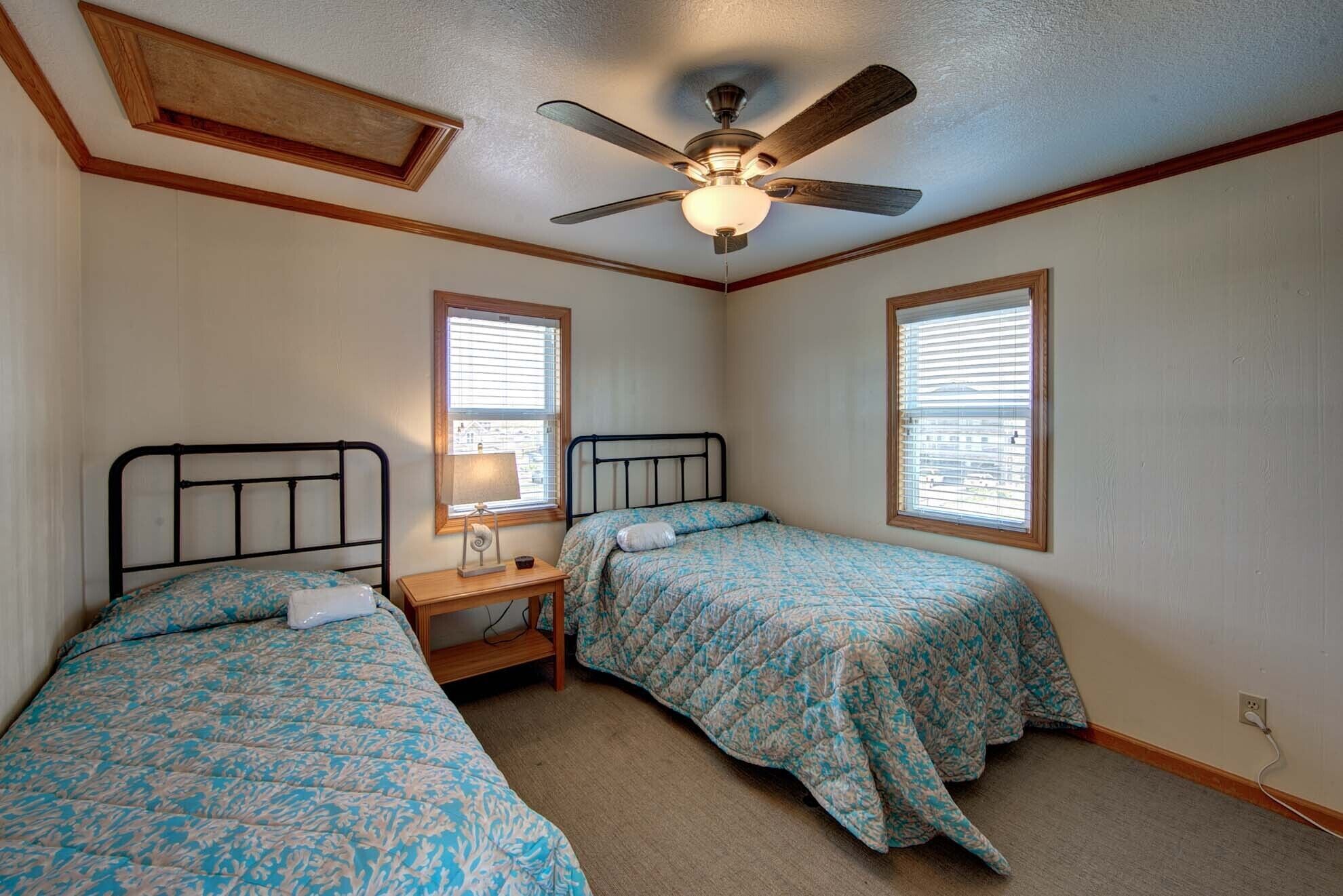 A bedroom with two beds, a ceiling fan, and two windows with blinds.