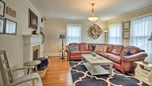 A living room with a brown leather sofa, a white coffee table, a patterned rug, a fireplace, and a chandelier. - Central Wadesboro Home: Walk to Downtown Shops! (Wadesboro)
