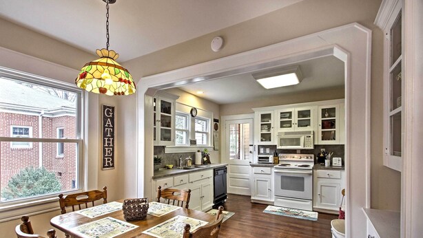 A kitchen with white cabinets, a dining table with chairs, and a hanging light fixture. - Central Wadesboro Home: Walk to Downtown Shops! (Wadesboro)