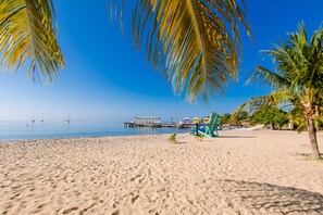 A beach with a clear blue sky, palm trees, and a pier in the background. - The Great Escape in Belize's Best Tourist Destinations!! (Placencia)
