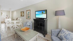 Een woonkamer met een televisie, een eettafel, stoelen, een bank en een kast.
