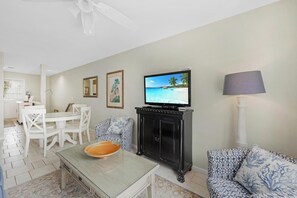 Ein Wohnzimmer mit Fernseher, Esstisch, Stühlen, einer Couch und einem Schrank.