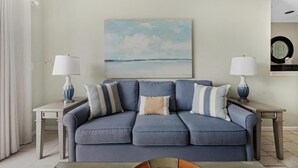 Een woonkamer met een grijze bank, twee bijzettafels met lampen, een schilderij van een strand en een houten salontafel.