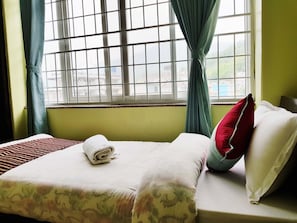 A neatly made bed with a rolled towel, a red pillow, and a white pillow.