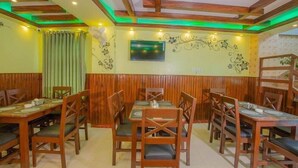 A restaurant with wooden paneling, a TV mounted on the wall, and a green-lit ceiling. - Hotel Arhant Inn (Pokhara)