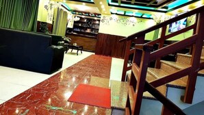 A hotel lobby with a marble floor, a reception desk, a staircase, and a wall with decorative elements. - Hotel Arhant Inn (Pokhara)