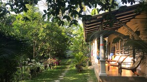 A garden pathway leading to a covered seating area with a pergola, surrounded by lush greenery and potted plants. - Villa Coconut - Hostel (Weligama)