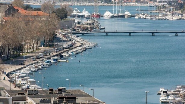 Ein Yachthafen mit zahlreichen Schiffen, eine Brücke, die über das Wasser führt, und Gebäude entlang des Ufers.
