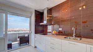 Eine moderne Küche mit einem großen Fenster, einem Balkon mit Korbmöbeln und Blick auf die Stadt.