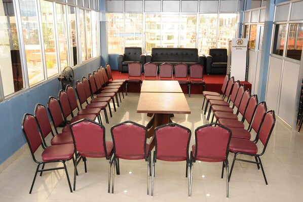 Un salón de conferencias con una larga mesa y sillas rojas dispuestas alrededor, un sofá en el centro y grandes ventanales con vistas a edificios.