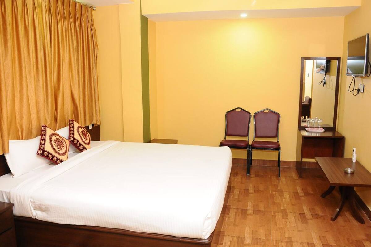 A hotel room with a bed, two chairs, a small table, a mirror, and a television.