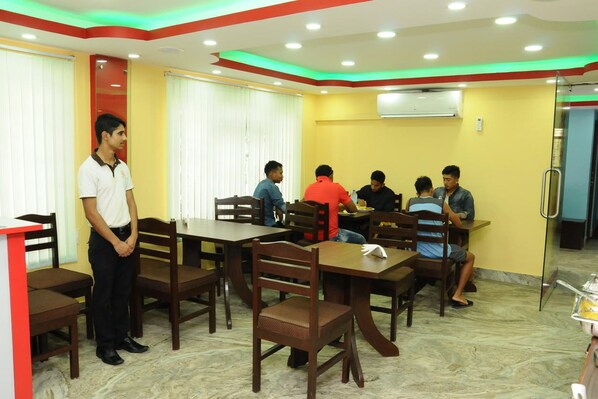 A dining area with multiple tables and chairs, an air conditioning unit on the wall, and a glass partition. - Rameshworam Hotel (Kathmandu)
