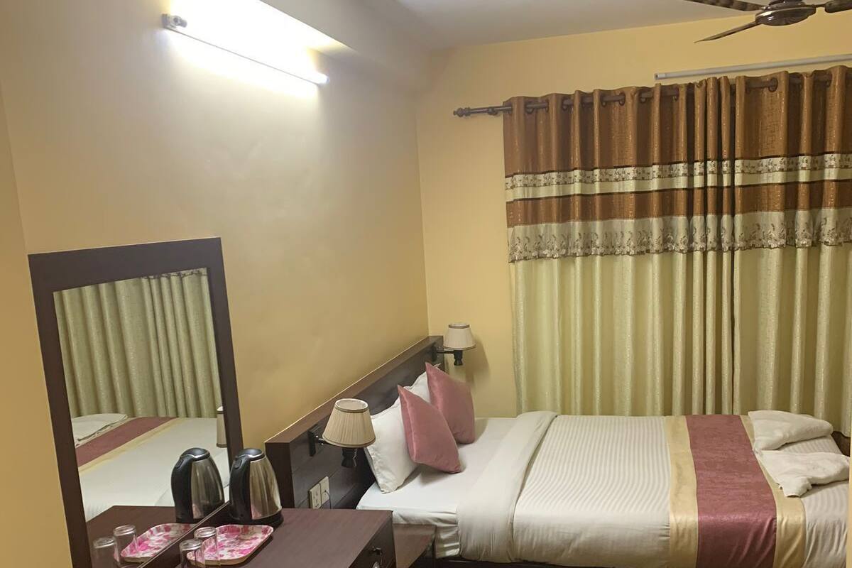 A hotel room with a bed, a desk with a mirror, a ceiling fan, and a window with curtains.