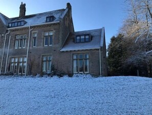 Un grand bâtiment à deux étages, doté de nombreuses fenêtres et d’un toit en pente, entouré de neige.