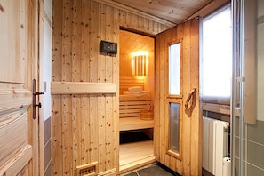 A wooden sauna room with a bench, a control panel, and a window.