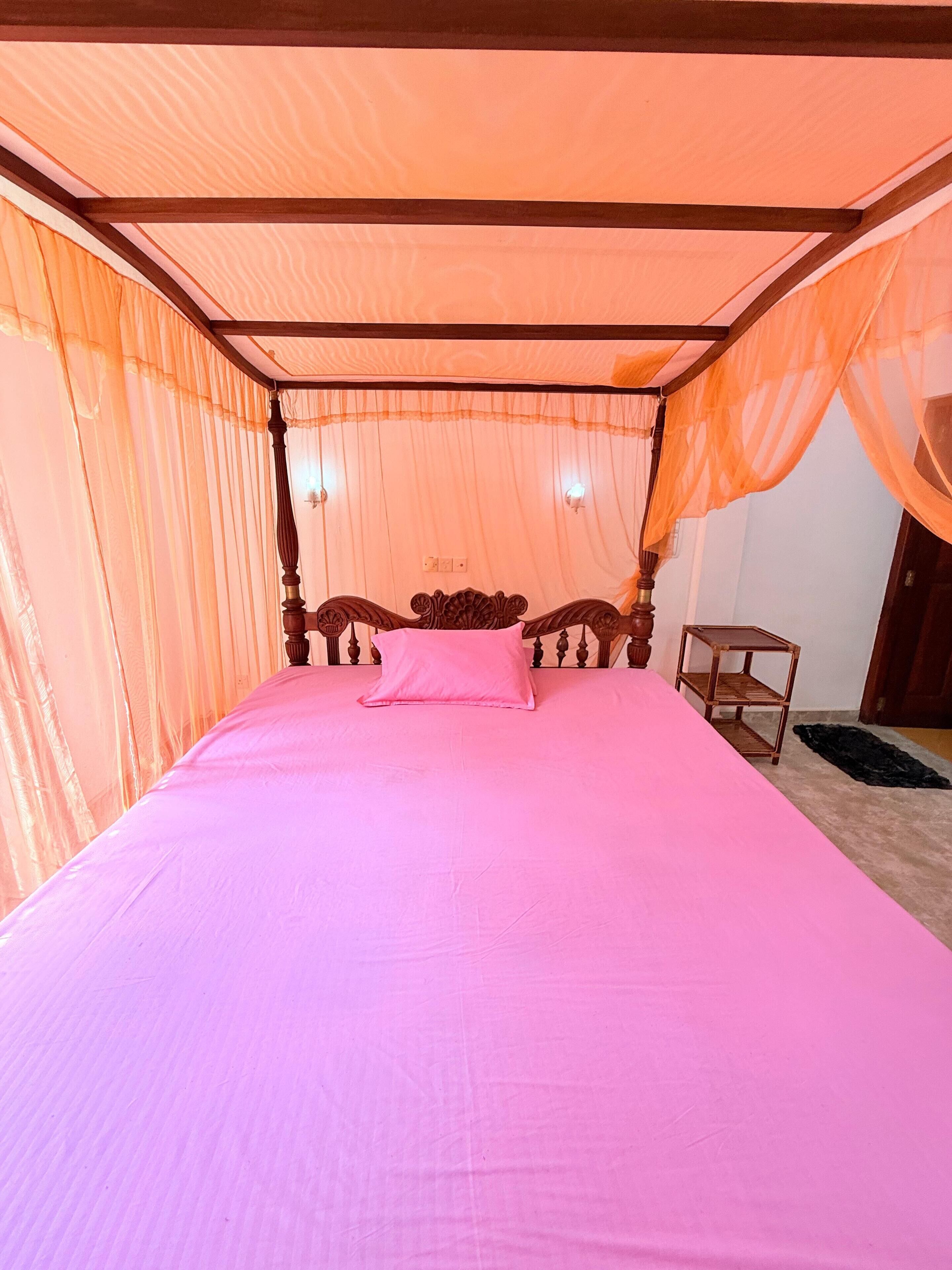 A bed with a canopy, a bedside table, and a lamp.