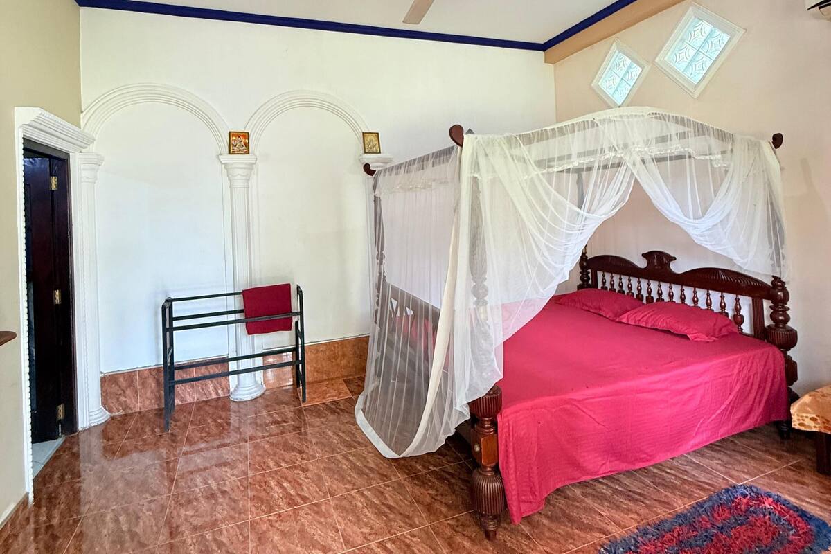 A bedroom with a bed under a canopy, a ceiling fan, and a red bedspread.
