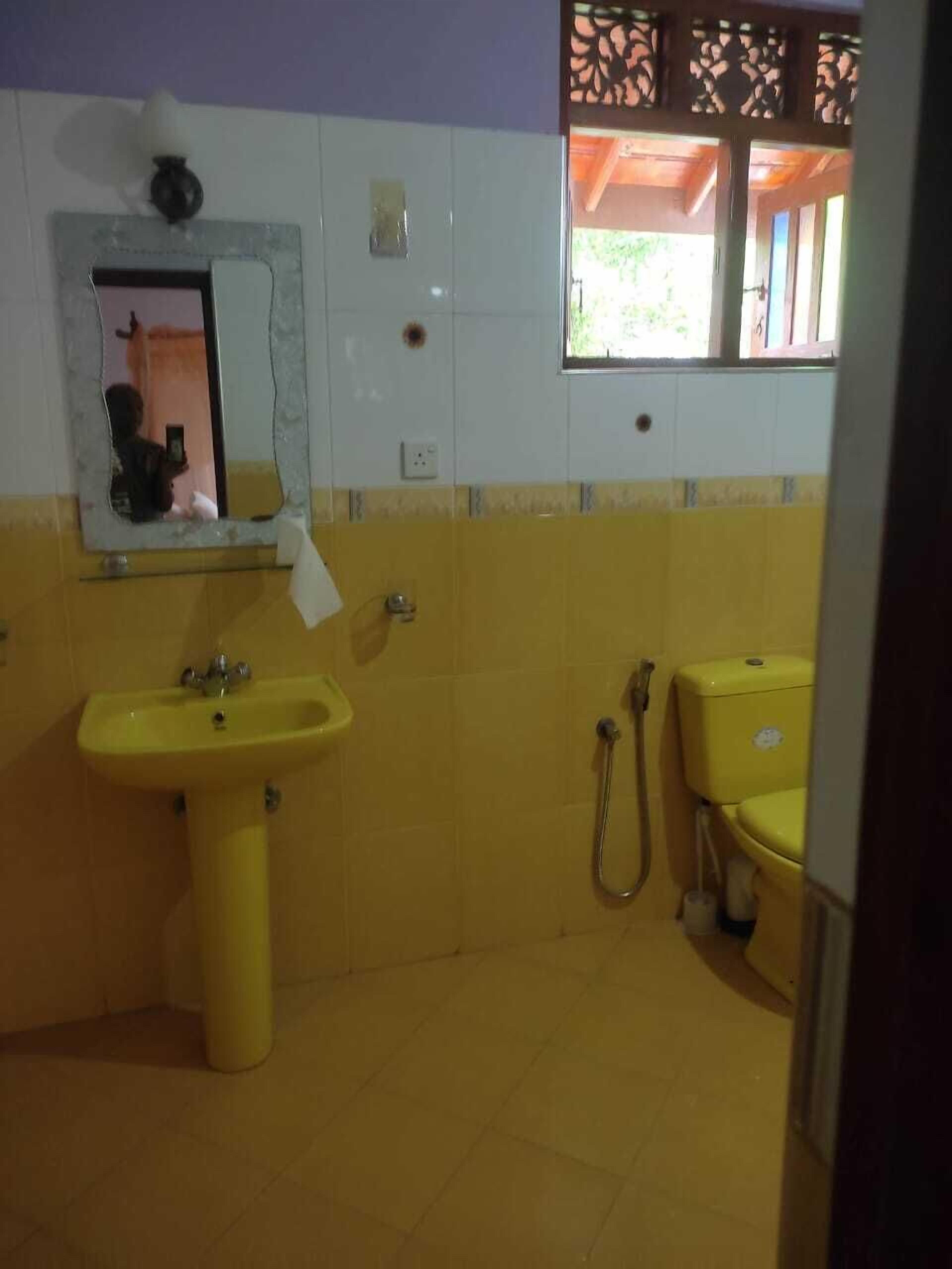 A bathroom with yellow tiles, a sink, a toilet, and a shower.