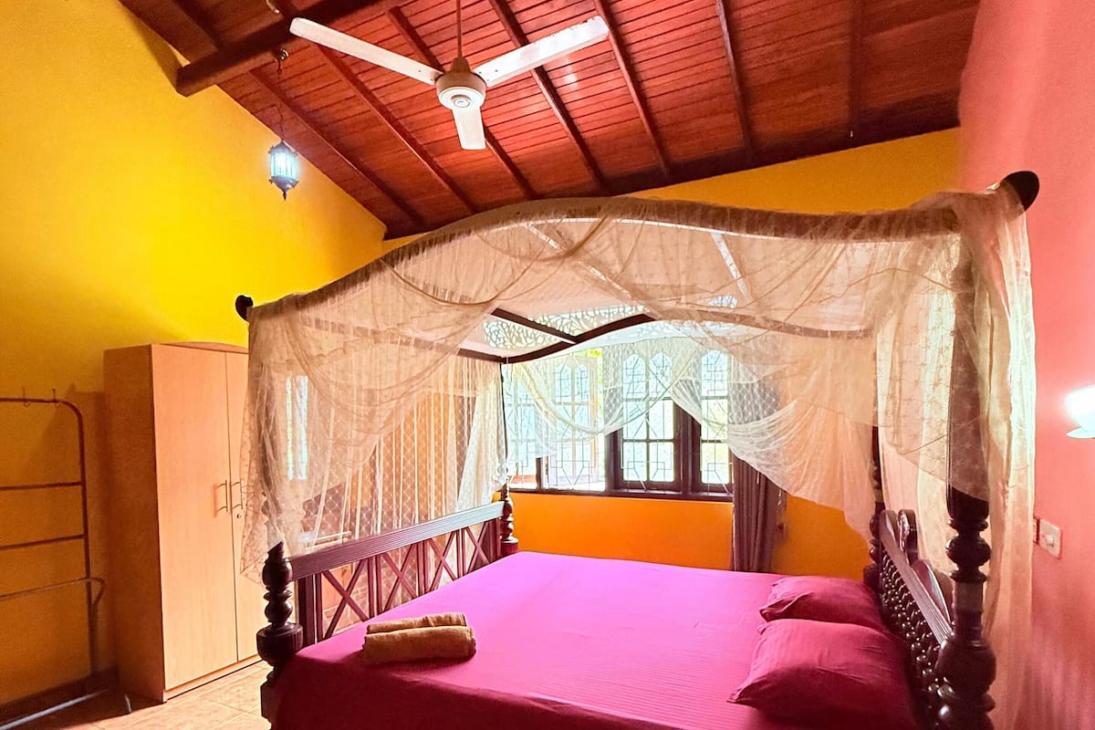 A room with a bed, a wooden ceiling, and a window.