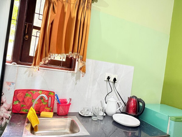 A kitchen with a sink, a window with curtains, a red fruit-themed cutting board, a kettle, and a toaster. - Utopia villa (Hikkaduwa)