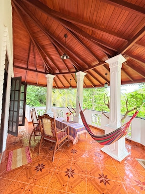 A covered outdoor area with a tiled floor, wooden furniture, and a hammock. - Utopia villa (Hikkaduwa)