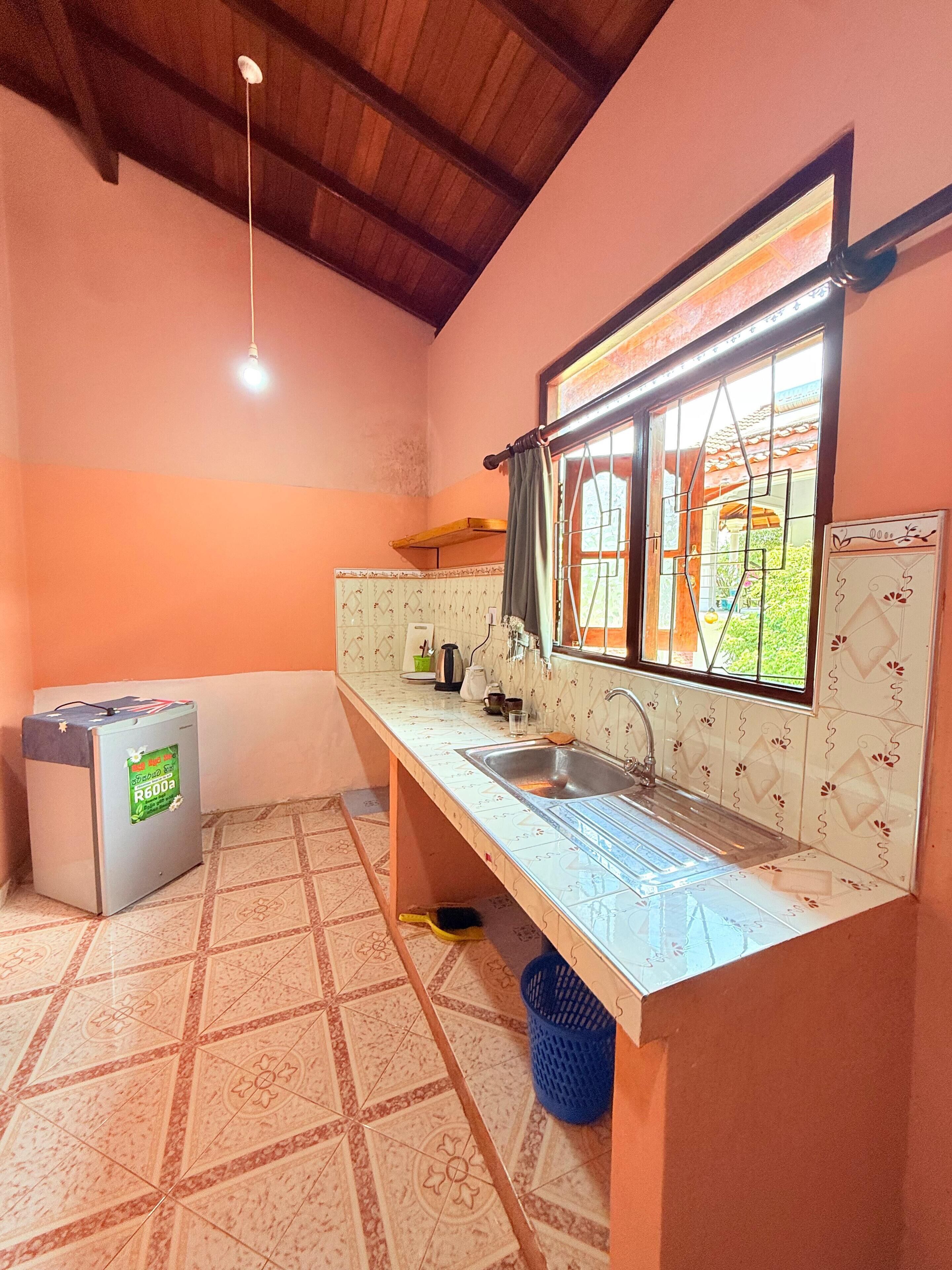 A compact kitchen with a sink, a small refrigerator, and a window with curtains.