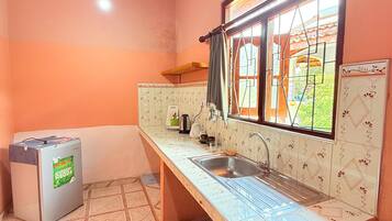 A compact kitchen with a sink, a small refrigerator, and a window with curtains.