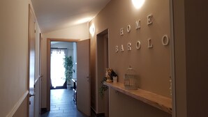 A hallway with a wooden shelf displaying decorative items, a wall with 'HOME BAROLO' letters, and a door leading to a bright room with a plant. - Barolo houses with large terrace and swimming pool for the whole family (SIRACUSA)