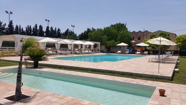 A swimming pool with lounge chairs and umbrellas, surrounded by trees and buildings. - Barolo houses with large terrace and swimming pool for the whole family (SIRACUSA)
