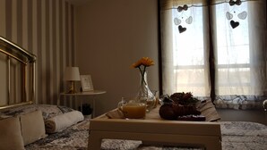 A cozy living room with a sofa, a coffee table with a glass of orange juice, a vase with flowers, and a window with heart-shaped decorations. - Barolo houses with large terrace and swimming pool for the whole family (SIRACUSA)