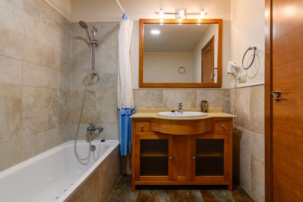 A bathroom with a bathtub, a wooden vanity with a sink, a mirror, and a shower.