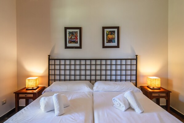 A double bed with white linens and two bedside lamps, a headboard with a grid pattern, and two framed pictures on the wall.