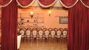 Un teatro con cortinas rojas, filas de asientos y un escenario.