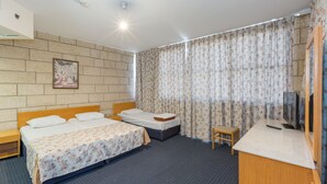 Habitación de hotel con dos camas, un escritorio pequeño, un televisor y una ventana con cortinas.