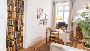 Ein Essbereich mit einem Tisch für zwei Personen, einem Bücherregal, gerahmten Bildern an der Wand und einer Lampe.